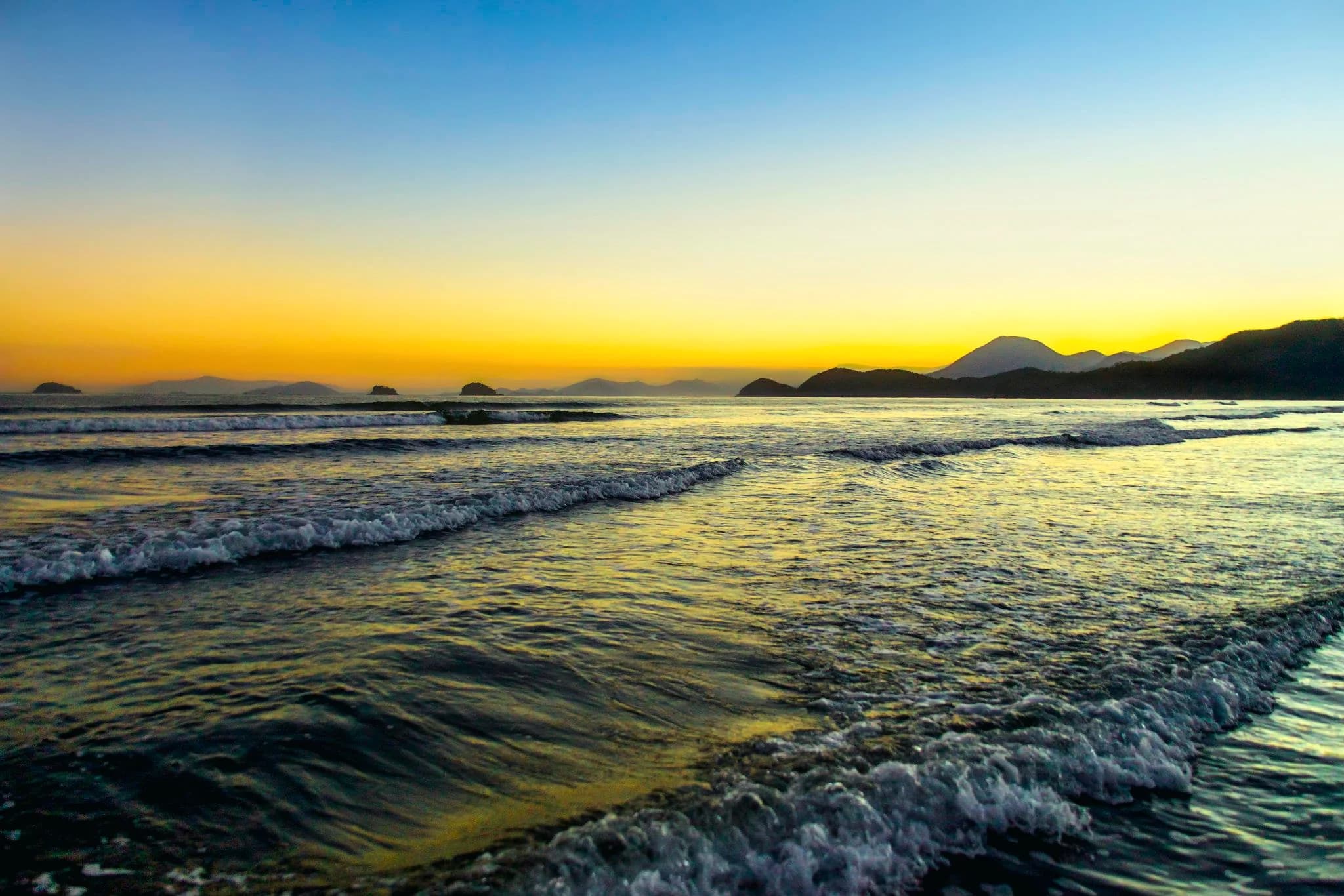 Pôr do sol dourado na Praia da Fazenda, em Ubatuba, com ilhas no horizonte